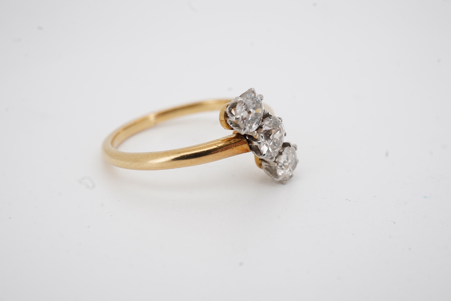 A mid to late 20th century yellow metal and three stone diamond set crossover ring, total diamond weight approx. 0.45-0.50ct, size K, gross weight 2.5 grams.